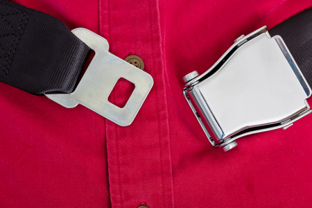 Unsafe transportation with an unclipped seatbelt around the waist of a male passenger in an aeroplane during a flight in a close up view on the open buckleの写真素材