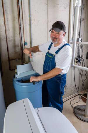 Hopeless home installer having trouble installing a new household water softener giving a thumbs down gesture with a rueful smileの写真素材