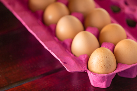 Pink recycled paper box of dozen eggs in close-up with selective focus, on dark lacquered wooden...