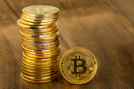 Single gold Bitcoin coin standing upright alongside a stacked pile in a concept of a digital or virtual cryptocurrency, online finances, and investment on wood with copy spaceの写真素材