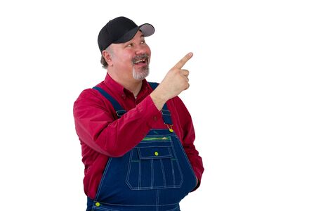 Pleased happy man in denim dungarees pointing up drawing your attention towards blank white copy space with a beaming smileの写真素材