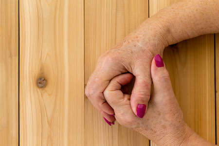 Clasped hands of senior woman in close up against wooden tableの写真素材