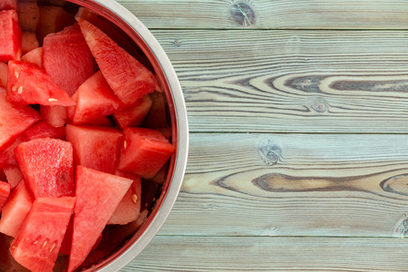 Chilled metal bowl full of diced fresh juicy watermelon for a refreshing summer dessert on a weathered pine wood picnic table with copy spaceの写真素材
