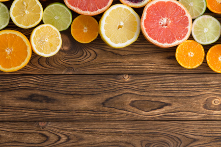 Curved border of a variety of colorful halved succulent fresh tropical citrus fruit on a rustic wood background with woodgrain and copy spaceの写真素材