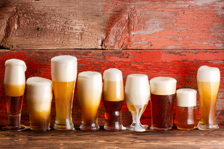 Multiple frothy lager beer pints on wooden bar bench top with a rustic timber background.の写真素材