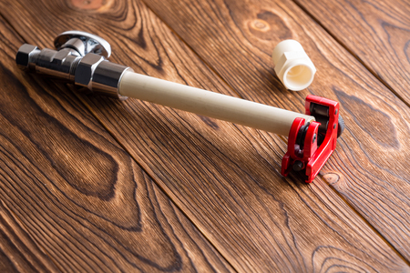 Length of plastic CPVC pipe for a plumbing installation or repair in a bright red pipe cutter over a wooden table with copy spaceの写真素材