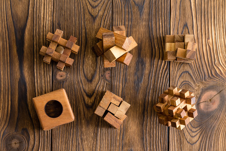 Six wooden puzzles of differing complexities arranged in two rows on a wood background with decorative woodgrainの写真素材