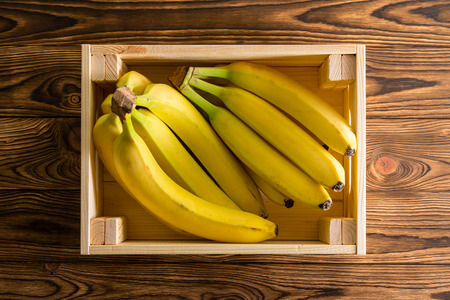 Wooden box with bunches of fresh ripe bananas or sweet plantains on a rustic wood table at an organic farmers market viewed close up top downの写真素材