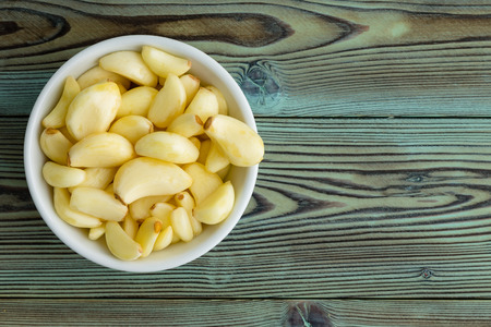 Freshly peeled aromatic garlic cloves in a generic white ceramic ramekin to the side on rustic woodの写真素材