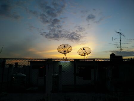 cityscape with parabolic satellite dishes at building roof and sunset backgroundの写真素材