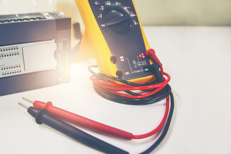 Multimeter with PLC placed on white table.