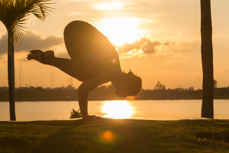Young woman practicing yoga on the park at sunset, Silhouette.の写真素材