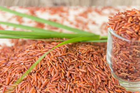 Red rice or Bruwn rice piled on a wooden floor and in a small glass.の写真素材