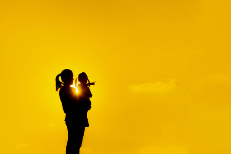 The family silhouette of the mother and child standing watch the sunset and the sky in orange in evening.の写真素材
