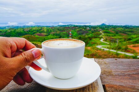White hot coffee mugs placed on a wooden floor with green fresh mountain and morning fog as...