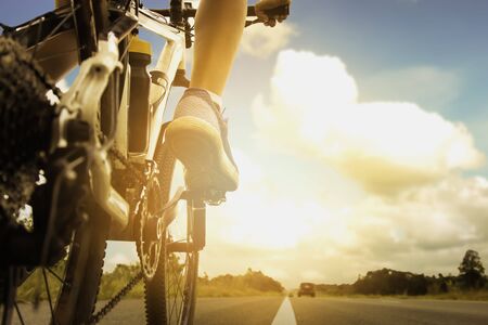 Shot from the back of a bicycle with a boy riding on a bicycle on the public road in the summer as a workout for a healthy body, a long road and a beautiful sky with the orange sun of the evening.の写真素材