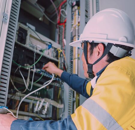 Engineer in yellow uniform, wearing a white safety helmet, checking communication system, big data...