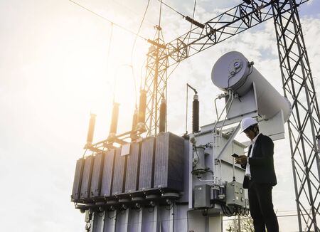 A low angle image of a businessman wearing a black suit, standing looking at a large power...