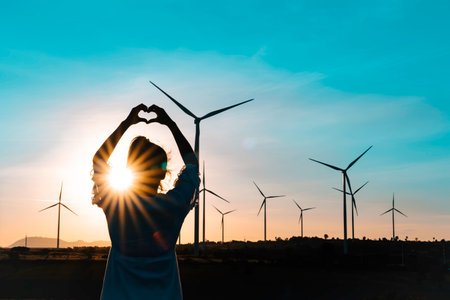 Wind turbines farm is an alternative electricity source, Concept of sustainable resources, Renewable energy concept, Girl standing and watching the sunset with wind generators turbines to backgrounds.の写真素材