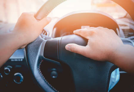 A man's hand is pressed to the horn of a car to warn vehicles that are not complying with traffic laws, which could pose a danger to his and other vehicles, as well as to the commuters.の写真素材