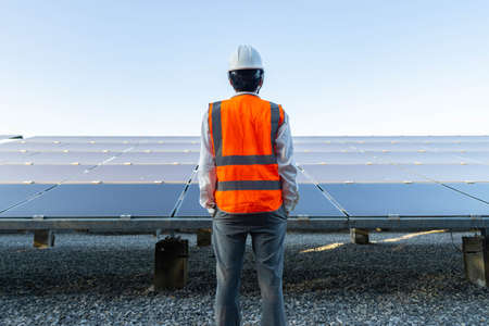 Engineer, wearing an orange reflective shirt, looks at the solar panel, Alternative energy to...