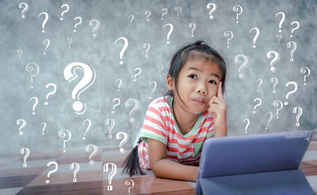 Asian little girl thinking with a question mark symbol in gray background. Kid ideas and brainstorm.の写真素材