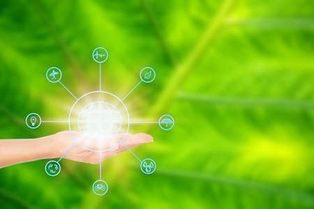 On the palm is a icon of the world. Surrounding is a source of renewable energy that is popularly used as an environmental concept. and global warming on green leaf background.の写真素材