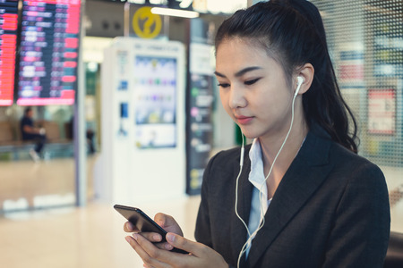 Young woman in international airport, checking her phone while waiting for her flightの写真素材