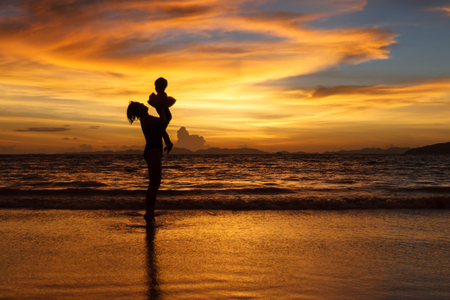 Mother  holding her child up in the sky at the beachの写真素材