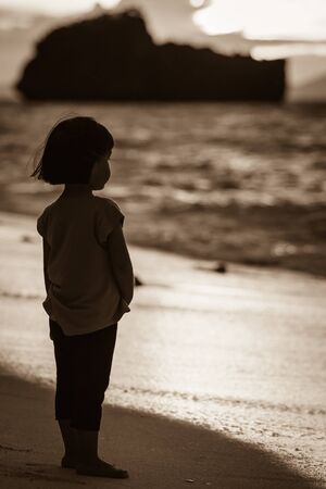 An Asian little girl standing alone on the beach facing to the seaの写真素材