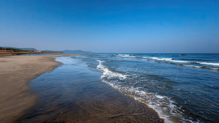 This stunning coastal landscape features gentle waves lapping against a serene sandy beach under a clear blue sky. Perfect for evoking a sense of tranquility and relaxation.の素材