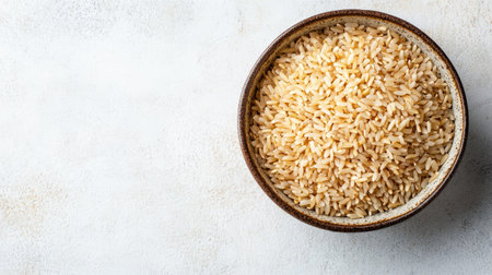 Brown rice in a ceramic bowl, top view with copy space on a light-colored surface, ideal for organic food promotionの素材