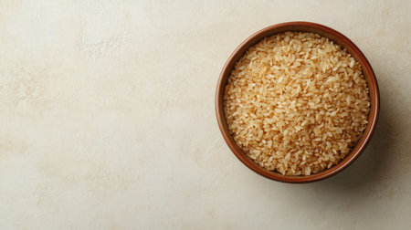 Brown rice in a ceramic bowl, top view with copy space on a light-colored surface, ideal for organic food promotionの素材