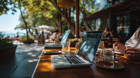 A vibrant outdoor workspace featuring laptops, drinks, and people enjoying a sunny day at a cafe, perfect for creative inspiration and relaxation.の素材
