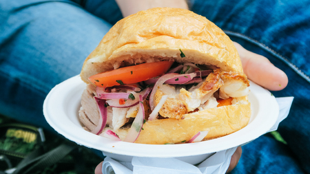 Chicharron bun, Peruvien pork sanwich on a man hand in Comida fest, Latin American street food....