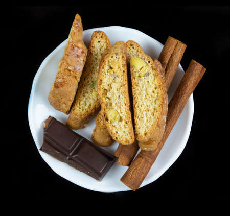 Cinnanon sticks, chocolate and bisquits in a white plate isolated over black backgroundの写真素材