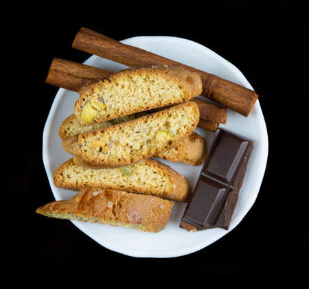 Cinnanon sticks, chocolate and bisquits in a white plate isolated over black backgroundの写真素材