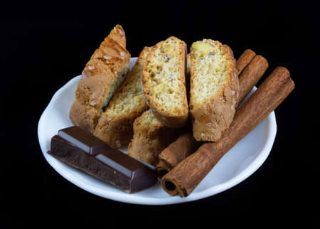 Cinnanon sticks, chocolate and bisquits in a white plate isolated over black backgroundの写真素材