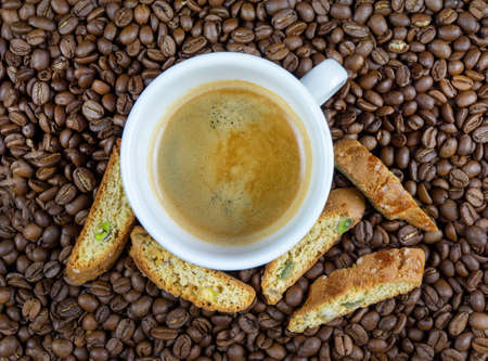 A coffee in white cup surrounded by coffee beans and bisquitsの写真素材