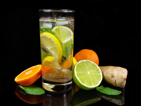 Glass of fresh lemonade and pieces of cut lemon fruits on black reflective backgroundの写真素材
