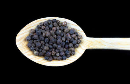 Black pipper in wooden spoon isolated on black backgroundの写真素材