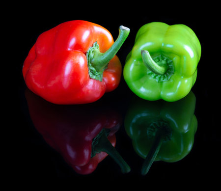 Red and green pappers on black reflective studio backgroundの写真素材