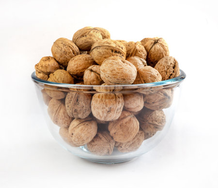 Whole solid walnuts in a glass bowl on white backgroundの写真素材