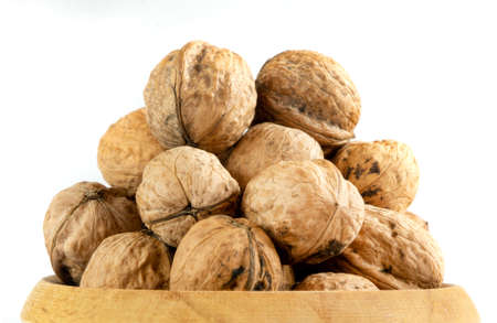 Whole solid walnuts in wooden bowl on white backgroundの写真素材