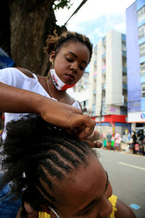 salvador, bahia, brazil - december 14, 2020: Young man is seen making afro moths on the hair of a black woman on the street in downtown Salvador.のeditorial素材