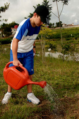 eunpolis, bahia brazil - june 19, 2009: child is seen using watering can to water plant in the city of Eunapolis.のeditorial素材