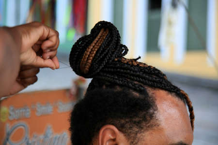 salvador, bahia, brazil - july 27, 2021: hairdresser is seen braiding tourist hair in Pelourinho, Historic Center of Salvador city.のeditorial素材