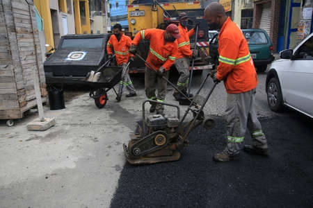 Salvador, Bahia, Brazil - February 18, 2022: Workers repair a hole in the asphalt of a street in the...