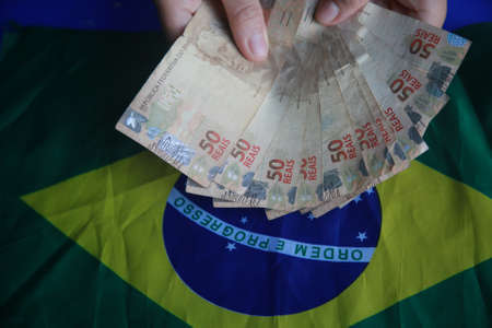 salvador, bahia, brazil - april 3, 2022: fifty reais banknotes next to a brazil flag.の写真素材
