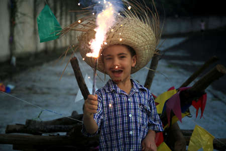 Salvador, Bahia, Brazil - June 22, 2022: Child wearing straw hat and releasing fireworks during SÃ£o JoÃ£o party in Salvador city.のeditorial素材
